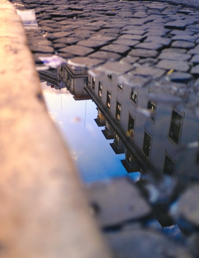 Reflection of buildings in a very small pool of water on a cobbled street