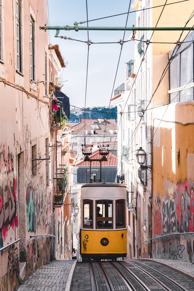 Narrow street in Lisbon with tram coming up and graffiti on either facade