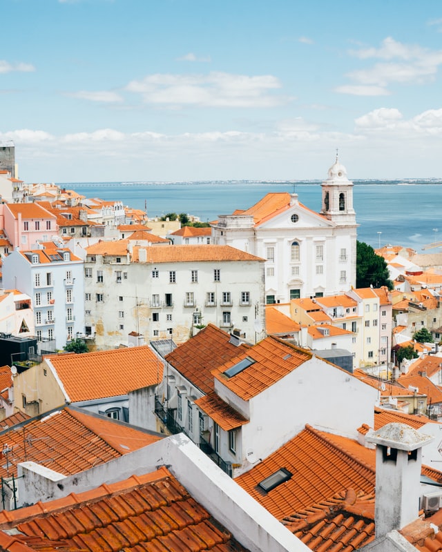 Picture over orange-tiled rooftops in Lisbon, with the sea in the backdrop