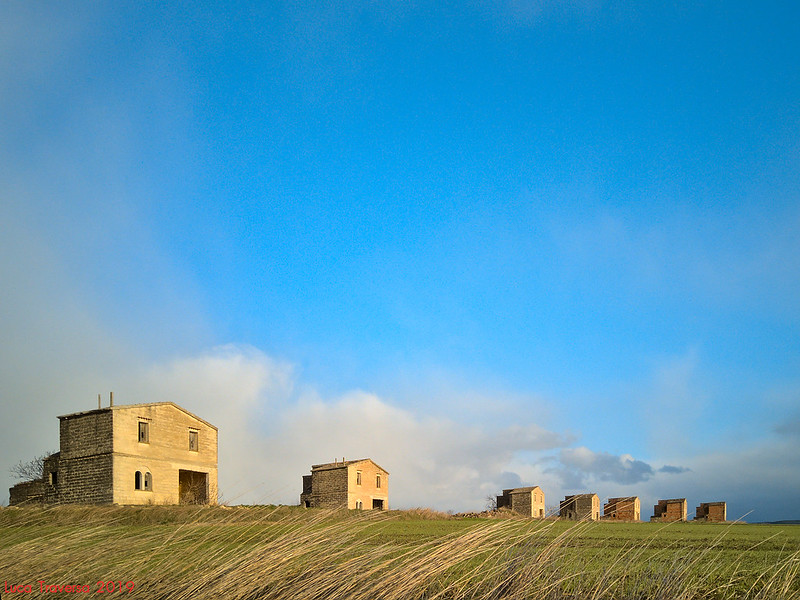 Rural landcape with row of stand-alone one-storey stone houses.