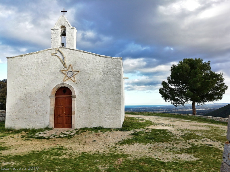 Picture of simple white-walled chruch with a star and pine tree with landscape and horizon in the background